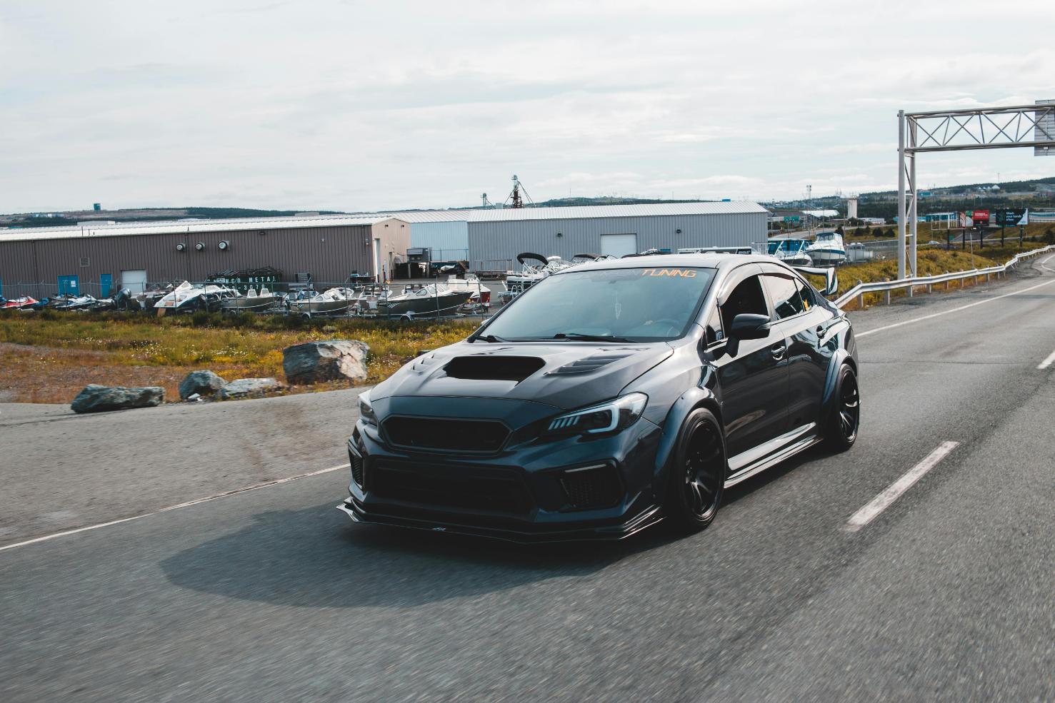 Heavily modified black Subaru WRX STI widebody driving on a road